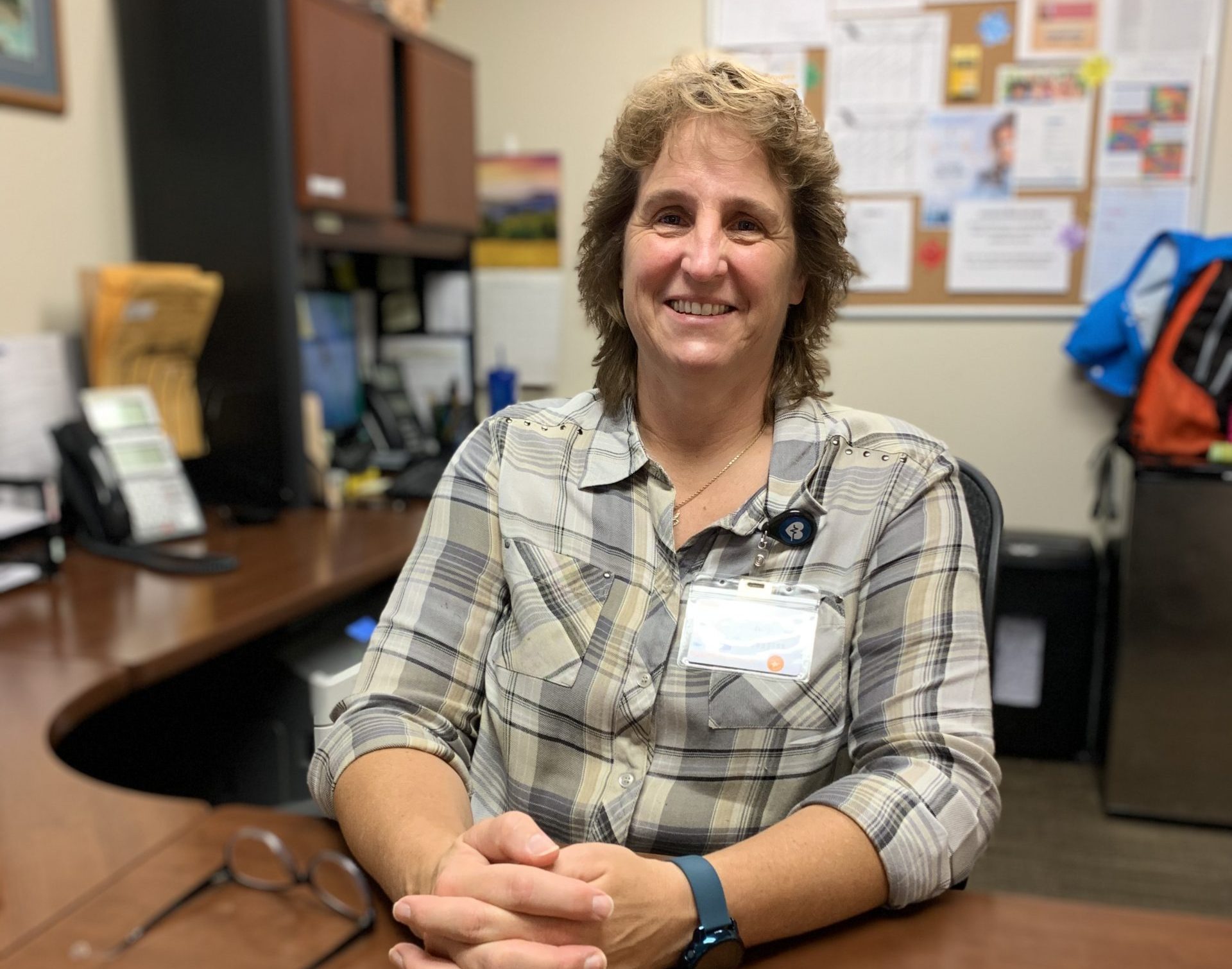 Wendy sits at a desk in an office with her hands clasped in front of her on top of the desk.